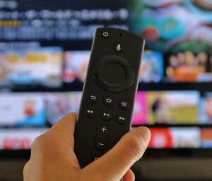 a man holding up the remote control of a FireStick TV
