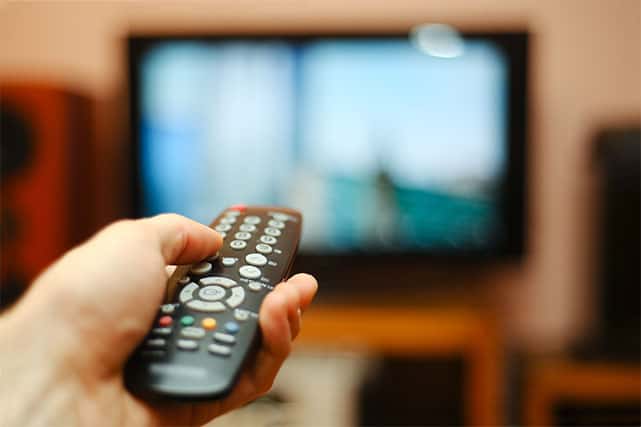An image featuring a person holding a tv remote and watching live television